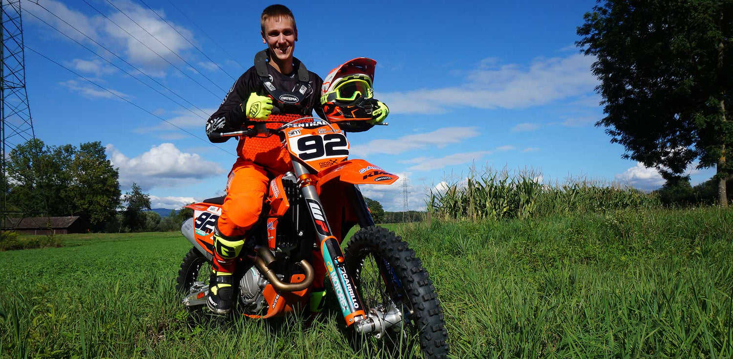 Ein junger Mann sitzt auf seinem Motocross Bike und lächelt in die Kamera